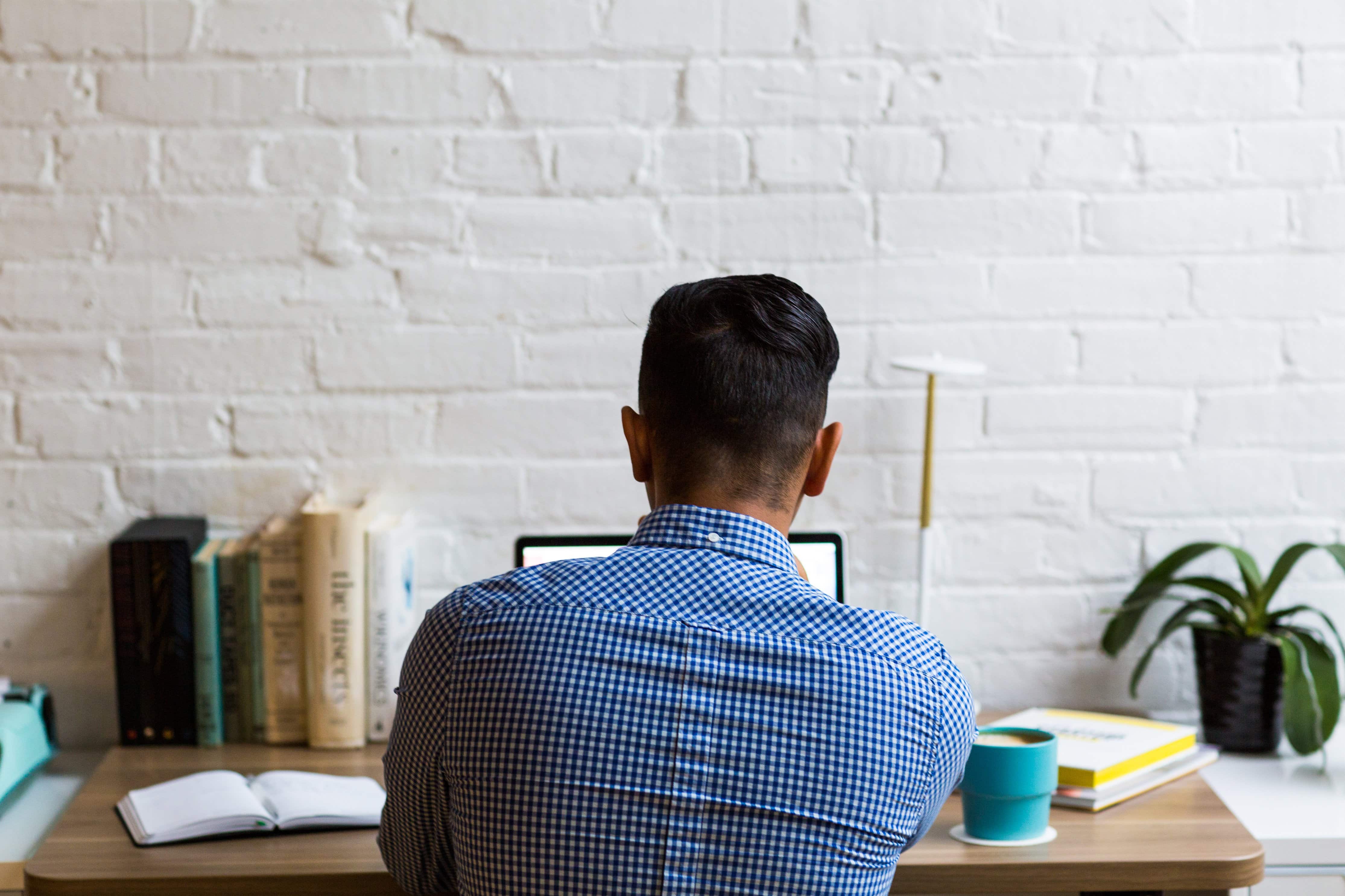 Man in blue dress shirt working on laptop with his back to the camera.