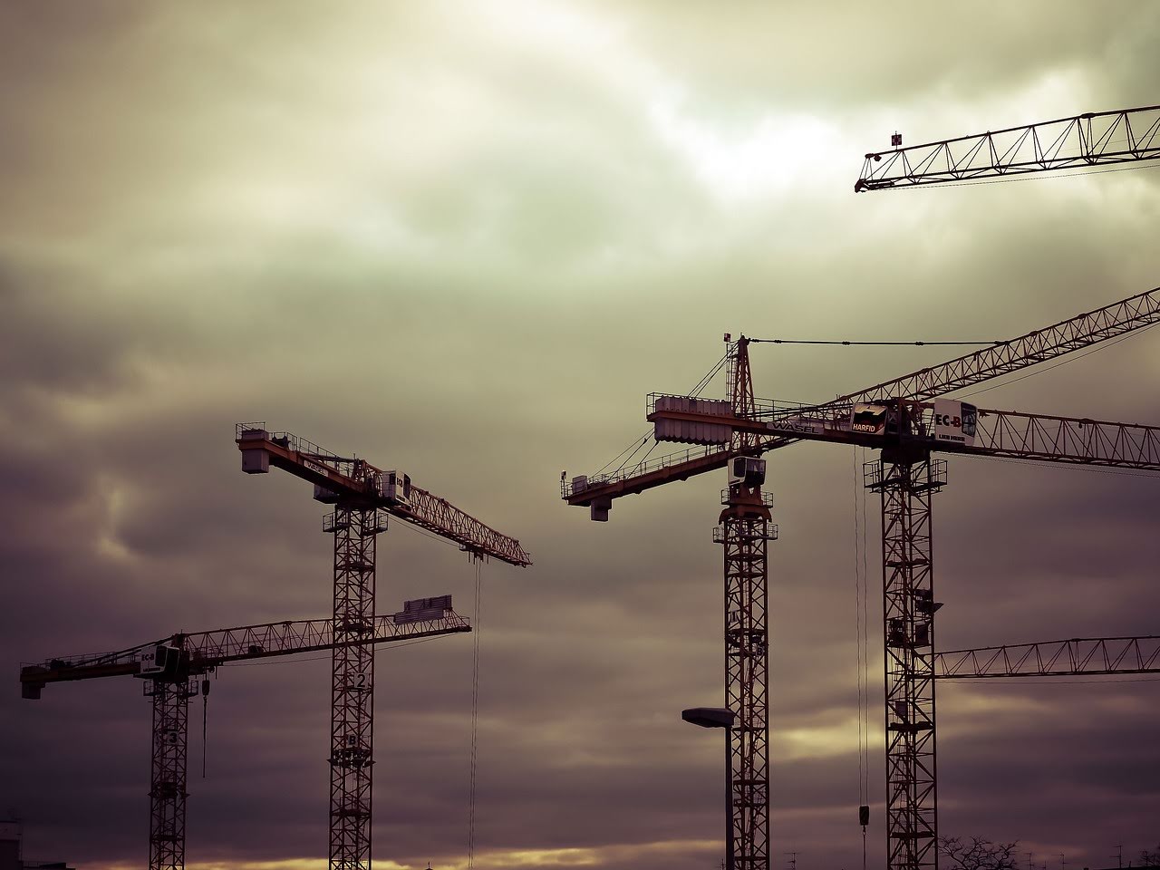a group of four construction cranes against a backdrop of a cloudy evening sky